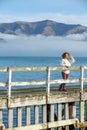 Beautyful asian woman resting is looks at the sea bay with houses and boats on a sunny day at Childrens bay, Akaroa, Canterbury, Royalty Free Stock Photo