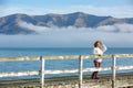 Beautyful asian woman resting is looks at the sea bay with houses and boats on a sunny day at Childrens bay, Akaroa, Canterbury, Royalty Free Stock Photo