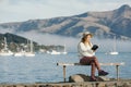 Beautyful asian woman resting is looks at the sea bay with houses and boats on a sunny day at Childrens bay, Akaroa, Canterbury, Royalty Free Stock Photo