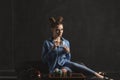 Beautyful girl in blue shirt drinks coffee on black background in studio. Multi-colored cupcakes on black tray