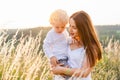 Beautyful woman with a little curly-haired boy in her arms stands in the middle of a field at sunset.