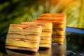 Bebinka on platter in sunlight, blurred leafy background, close-up. Bibik, the national Goan pie, cut into slices. Multi-layer Royalty Free Stock Photo