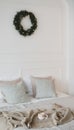 Bed with beige knitted plaid and a cup. Interior of stylish cozy bedroom with wreath on the wall. Christmas, New year home decor