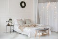 Bed with beige knitted plaid and a cup. Interior of stylish cozy bedroom with wreath on the wall. Christmas, New year home decor