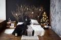 a bed with black and white linens against a dark wall with tree branches near the background and a garland. Christmas tree decorat