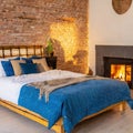 Bed with blue pillow and coverlet near fireplace. Loft interior design of modern bedroom with brick wall
