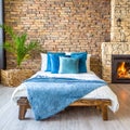 Bed with blue pillows and coverlet near fireplace against white brick wall. Loft, scandinavian interior design of modern bedroom Royalty Free Stock Photo