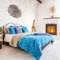 Bed with blue pillows and coverlet near fireplace against white brick wall. Loft, scandinavian interior design of modern bedroom Royalty Free Stock Photo