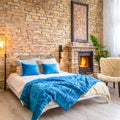 Bed with blue pillows and coverlet near fireplace against white brick wall. Loft, scandinavian interior design of modern bedroom Royalty Free Stock Photo