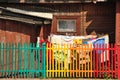 Bed linen and clothes are drying outside a wooden house behind a colourful fence