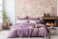 Bed with pillows and coverlet near fireplace against brick wall. Loft, scandinavian interior design of modern bedroom. Royalty Free Stock Photo