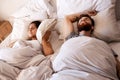 Bed, snoring and sleeping couple, frustrated woman or person with husband noise, problem and cover ears with pillow Royalty Free Stock Photo