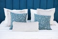 Bed with a soft blue velvet headboard and pillows in shades of beige and blue with a pattern. Close-up photo