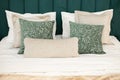 A bed with a soft green velvet headboard and pillows in shades of beige and green with a pattern. Close-up photo