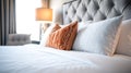 A bed with a white comforter and two pillows, one of which is orange Royalty Free Stock Photo