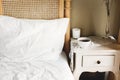 Bed with white sheets and vintage nightstand with white cup of coffee or tea in hotel room or provence home bedroom. Space for