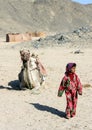 The bedouin girl walking alone in the desert against the background of a lying camel and hills.