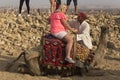 A Bedouin puts a white woman on a DROMEDARY camel.