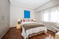 Bedroom with a double bed with colorful cushions on white pillows, a white chest of drawers with a gray blanket, a large window Royalty Free Stock Photo