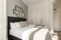 Bedroom with a double bed with a headboard upholstered in black quilted fabric, a white wooden built-in wardrobe and a mirror