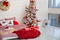 Bedroom interior with Christmas pillows, bed linen and red plaid. Cozy Decorated bedroom for Christmas holidays with tree and gift