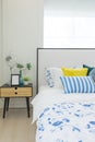 Bedroom interior with striped pillow on bed and bedside table lamp with picture frame on it.