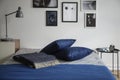 Bedroom interior with a warm wool blanket and navy blue pillows on a double bed by a white wall