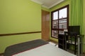 bedroom with small dark wooden bed with brown blanket with red trim,