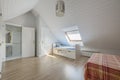 Bedroom with white cabinet doors, bed with striped bedspread, sloping ceilings and youthful bed with drawers, skylight in the Royalty Free Stock Photo