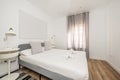 Bedroom with white and gray furniture, double bed with fabric headboard and white ederedon, curtains on the window and wooden Royalty Free Stock Photo