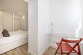 Bedroom with white wooden headboard, gray and pink cushions, white wooden bed, white glass and metal desk and built-in wardrobe Royalty Free Stock Photo