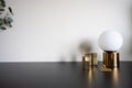 Bedroom working corner decorated with hexagon gold stainless vase and gold circular lamp on black working table with beige wall in
