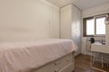 Bedroom with a youth bed with drawers next to a desk with a stool and a matching wardrobe