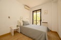 bedroom with a youth bed with gray cushions, matching bedspread, wooden floors and a balcony overlooking a garden