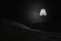 A bedside table and a burning lamp stands on it near the bed in a dark room. Hotel number. Place for text Royalty Free Stock Photo