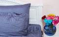 Bedside table with vase of flowers roses and bedroom fresh air. Bed with blue linens, blanket, pillows for comfortable sleep time