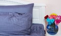 Bedside table with vase of flowers roses and bedroom fresh air. Bed with blue linens, blanket, pillows for comfortable sleep time