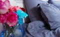 Bedside table with vase of flowers roses and bedroom fresh air. Bed with blue linens, blanket, pillows for comfortable sleep time