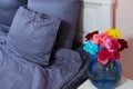 Bedside table with vase of flowers roses and bedroom fresh air. Bed with blue linens, blanket, pillows for comfortable sleep time