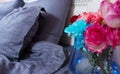 Bedside table with vase of flowers roses and bedroom fresh air. Bed with blue linens, blanket, pillows for comfortable sleep time