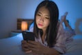 Bedtime lifestyle portrait of young beautiful and thoughtful sweet Asian Korean girl in pajamas enjoying relaxed with hand phone