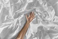 Hand of woman lying on rumpled bed sheet