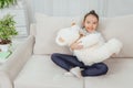 Cute small girl sitting on the sofa in lotos position, lulling her white teddy-bear. Royalty Free Stock Photo