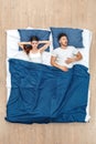 Bedtime. Young man sleeping yawning while woman covering ears concerned under blanket on bed top view Royalty Free Stock Photo