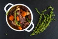 Beef Bourguignon in a white soup bowl on black stone background, top view.