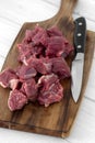 Beef brisket, diced cubed, on a wooden chopping board with a knife.