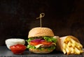 Beef burger, french fries, sauce on a black slate plate on a dark background, fast food, homemade hamburger Royalty Free Stock Photo