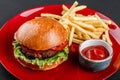 Beef burger and french fries with tomato sauce on red plate over dark background. Unhealthy food Royalty Free Stock Photo