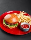 Beef burger and french fries with tomato sauce on red plate over dark background. Unhealthy food Royalty Free Stock Photo