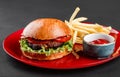 Beef burger and french fries with tomato sauce on red plate over dark background. Unhealthy food Royalty Free Stock Photo